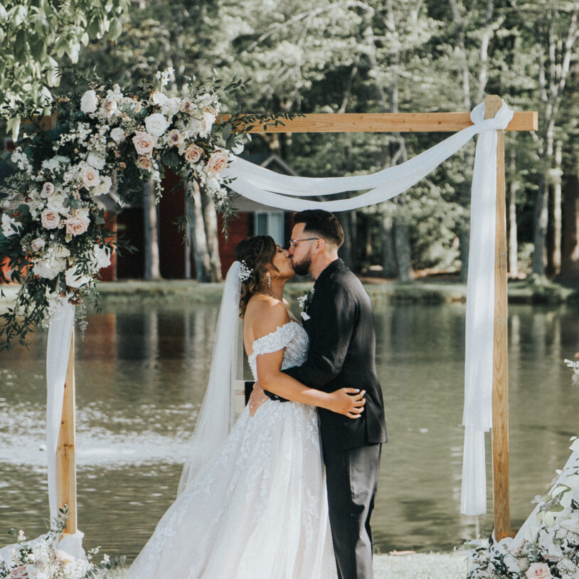 Wedding couple with arbor and lake in the background at Poconos wedding venue