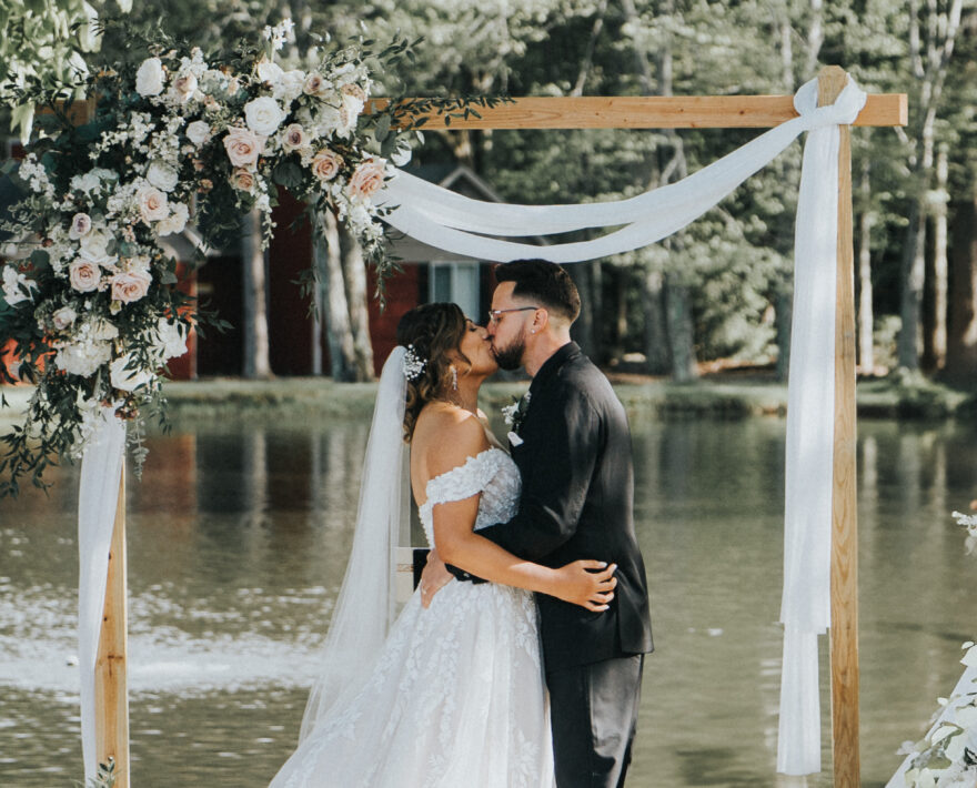 Wedding couple with arbor and lake in the background at Poconos wedding venue